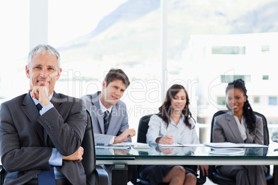 Mature manager sitting with his hand on his chin while his team