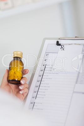 Hand holding bottle of drugs next to a clipboard