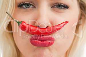 Cheerful woman placing a chili between her nose and her mouth