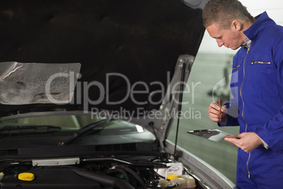 Mechanic looking at a car engine while holding a clipboard