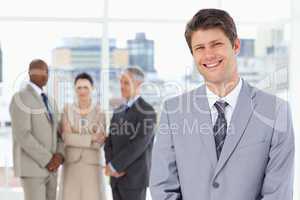 Young smiling manager standing upright with his team behind him