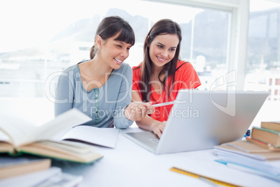 Two girls smiling as they use the laptop as one girl points at s