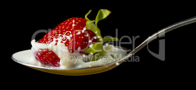 red, ripe strawberry falling in spoon with milk