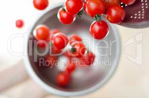 Cherry Tomatoes Tumbling From Metal Colander Into Metal Pan