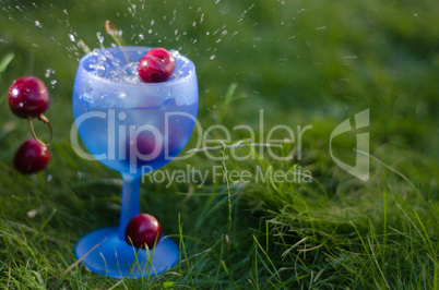 cherries dropping into blue glass of liquid
