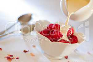 Cream pouring from a jug over fresh rasberries