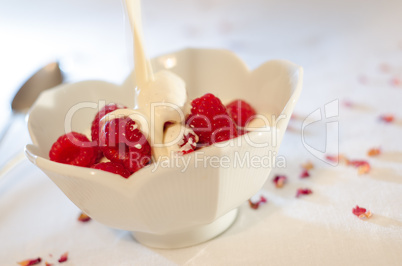 Cream pouring from a jug over fresh raspberries