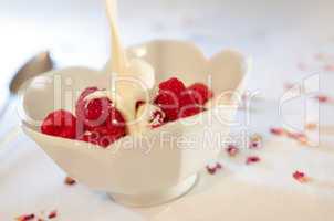 Cream pouring from a jug over fresh raspberries