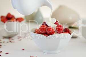 cream pouring from a jug over fresh strawberries