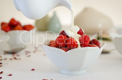 cream pouring from a jug over fresh strawberries