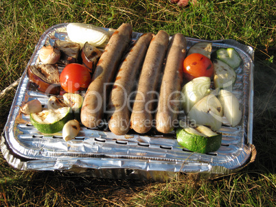 Einweggrill mit Gemüse und Bratwürsten