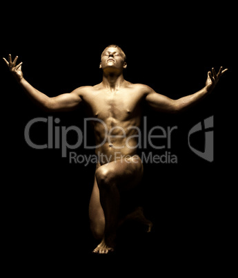 Strong man posing nude in dark with gold skin