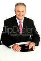 Senior businessman sitting with tablet on desk