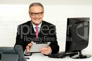 Aged businessman in glasses using tablet