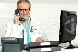 Aged doctor attending call in front of lcd screen