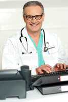 Smiling physician in eye wear typing on keyboard