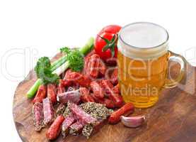 mug of beer and an assortment of salami and vegetables on a cutt