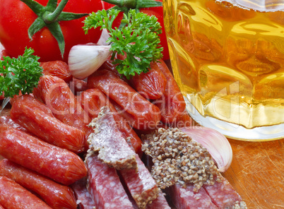 mug of beer and an assortment of salami and vegetables on a cutt