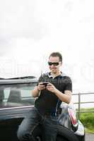 Happy man using his mobile outside his car
