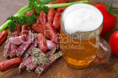 mug of beer and an assortment of salami and vegetables on a cutt