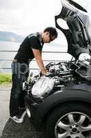 A young man fixing his car up the hills