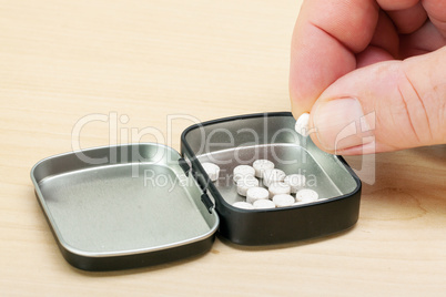 Hand taking a tablet from the tin box