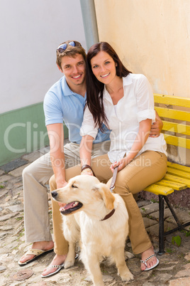 Happy couple with dog sitting yellow bench