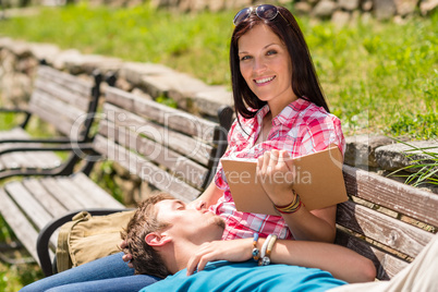 Woman reading book on bench man resting