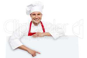 Handsome chef pointing at white billboard