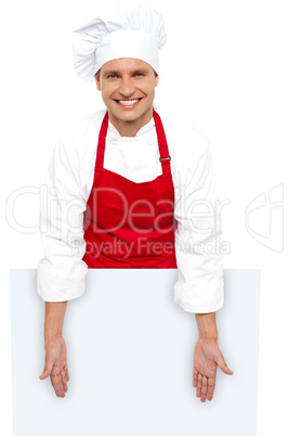 A smiling chef posing behind white billboard