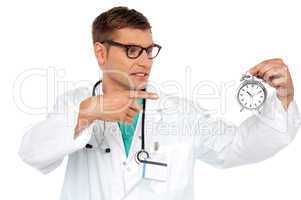 Shocking young doctor pointing at alarm clock
