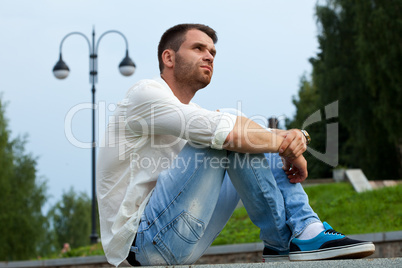 Young tired man sit on border in summer park