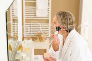 Senior woman apply make-up powder in bathroom