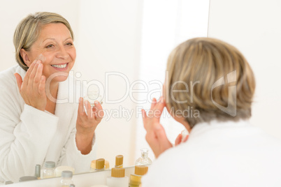 Mature woman apply cream looking bathroom mirror