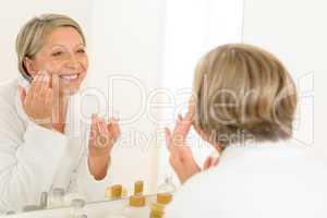 Mature woman apply cream looking bathroom mirror