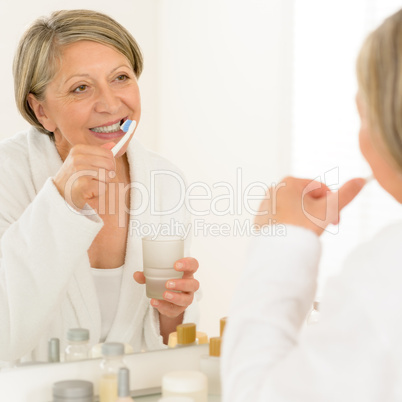 Senior woman brushing teeth bathroom mirror reflection