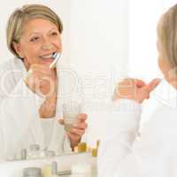 Senior woman brushing teeth bathroom mirror reflection
