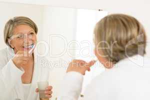 Mature woman brushing teeth look bathroom mirror