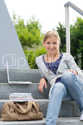 Young student sitting on university steps laptop