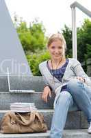 Young student sitting on university steps laptop