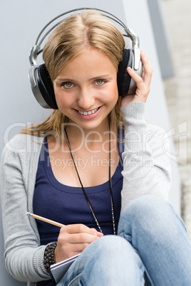 Young woman taking notes listening to music