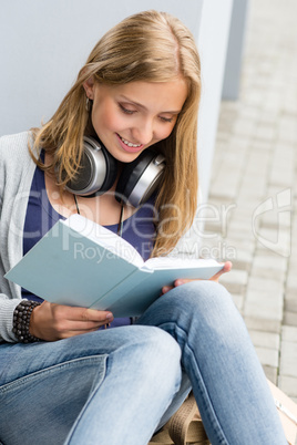 Smiling young student reading book outside school