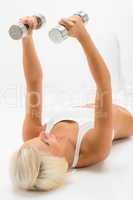 Fitness woman lifting dumbbells lying white floor