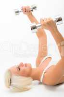 Fitness woman lifting dumbbells lying white floor