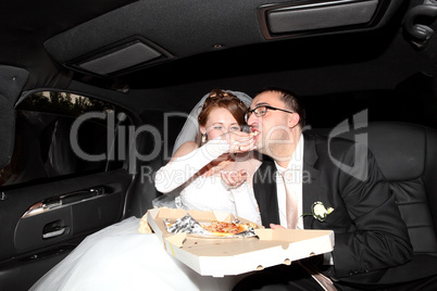 bride and groom eating pizza in the limousine