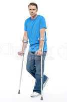 Painful expression by young man walking with help of crutches