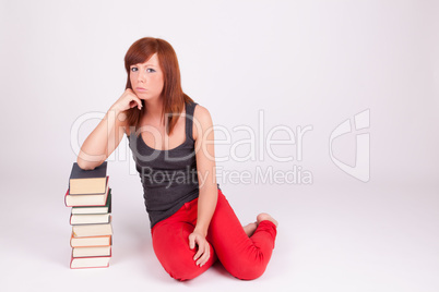 Eine junge Frau sitzt auf dem Boden neben einem Bücherstapel