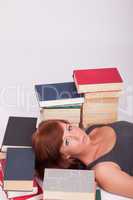 Eine junge Frau liegt auf dem Boden umgeben von vielen Büchern