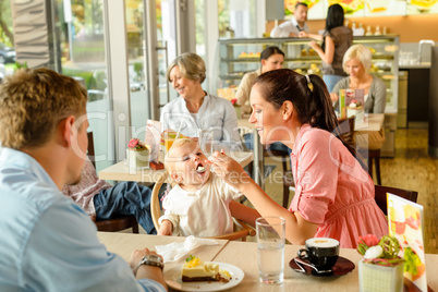 Father and mother feeding child cake cafe