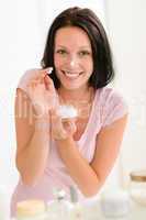 Smiling woman put moisturizer cream in bathroom